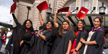 Graduating students wearing their graduation gowns outside the Usher Hall in Edinburgh, holding their certificates