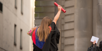 Graduating student facing away from the camera holding her scroll in the air in celebration