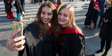 Two students taking a selfie together in their graduation gowns